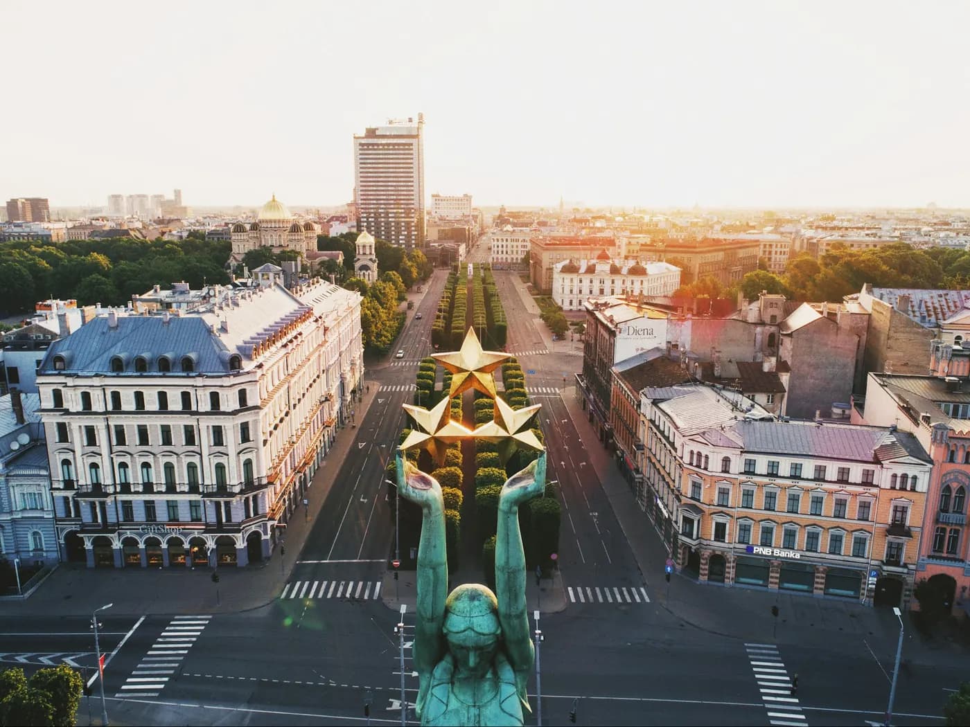 Rīga: Brīvības piemineklis ar trim zelta zvaigznēm virs bulvāra saullēktā